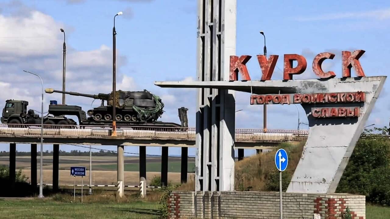 A convoy of military vehicles passes over a bridge with Russian text reading "Kursk". 