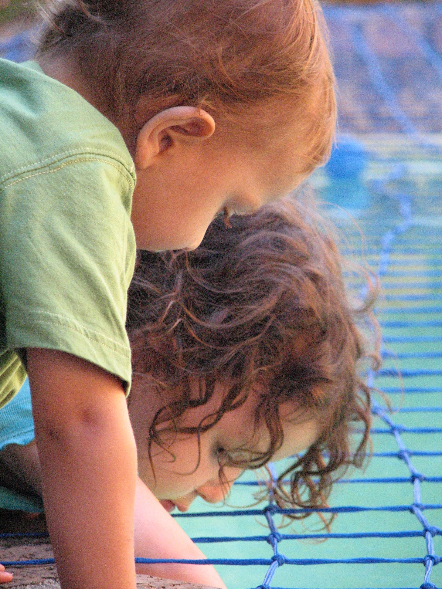 two young children peering into a pool with intent concentration