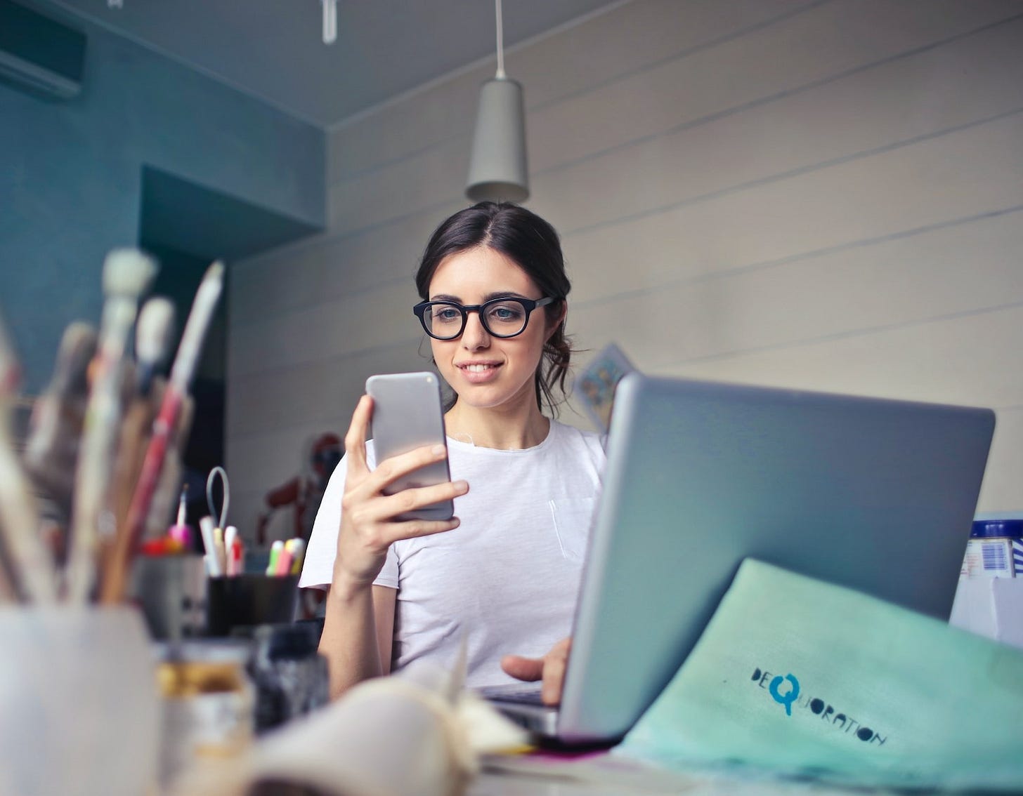 Woman in white facing a laptop and reading from a phone