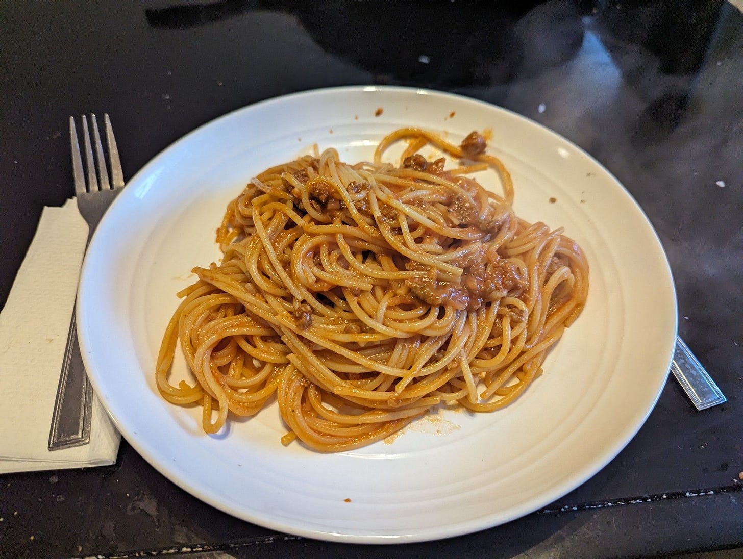 Spaghetti in a hot sausage cream sauce on a white plate on a black table