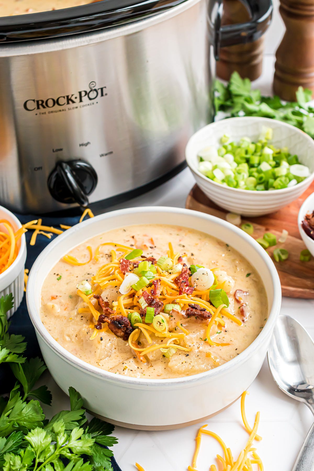 A bowl of potato soup garnished with shredded cheddar, bacon bits and green onions.