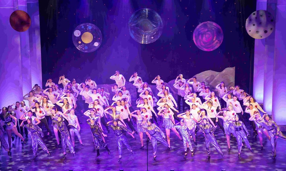 large group of children on stage with space suits and planets in the backdrop