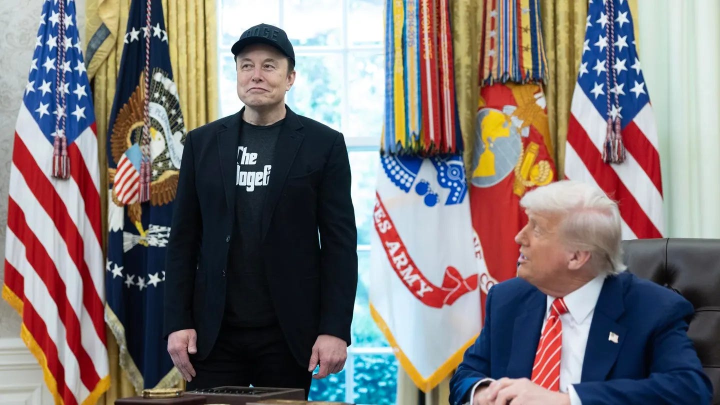 Donald Trump looking up at Elon Musk from his desk. Musk standing smugly beside an American flag in a black DOGE hat, black blazer, and The Dogefather t-shirt like an asshole.