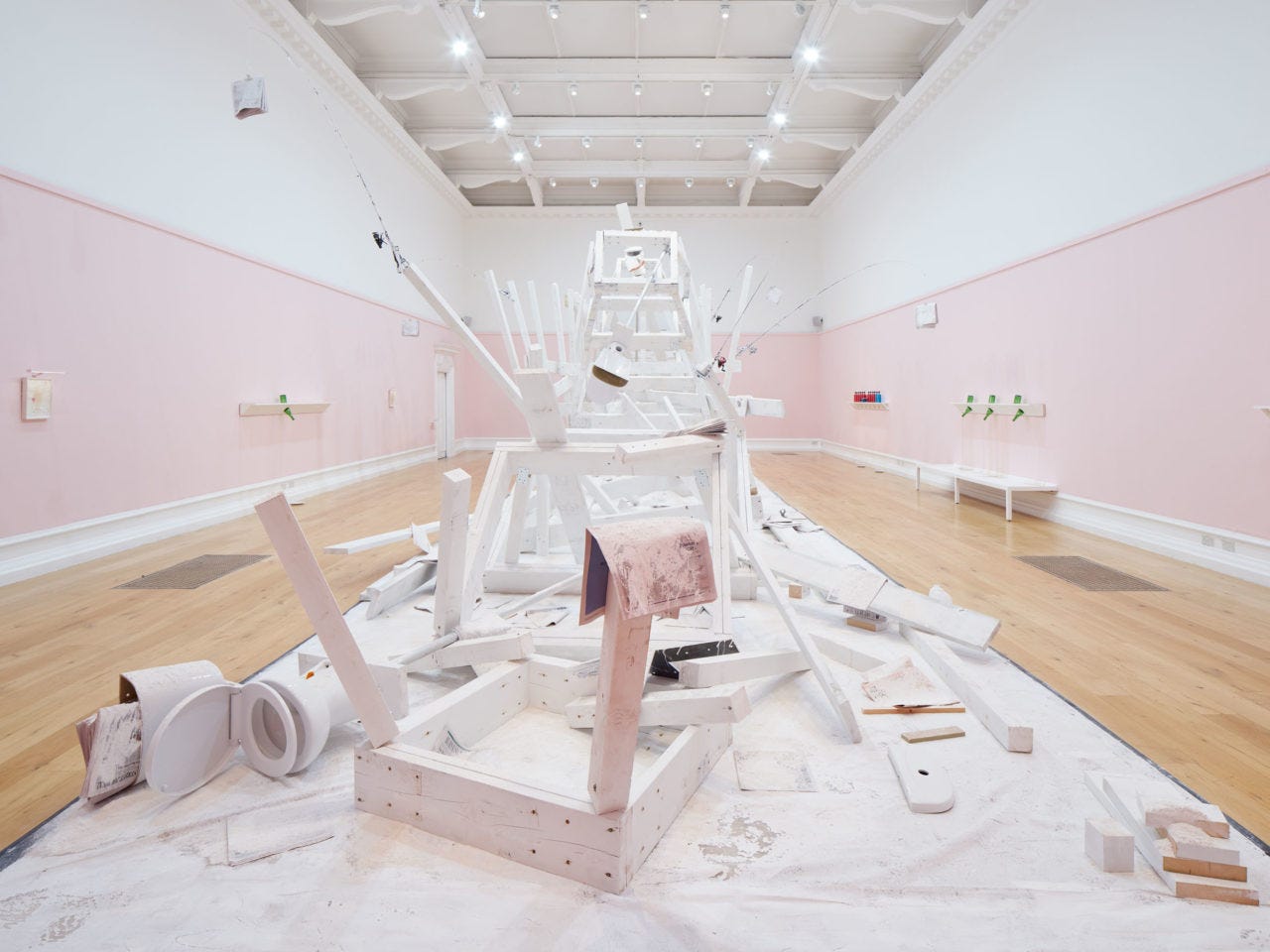 A wooden installation by artist Pope.L painted white and covered in flour in the centre of a large gallery with pink and white walls.