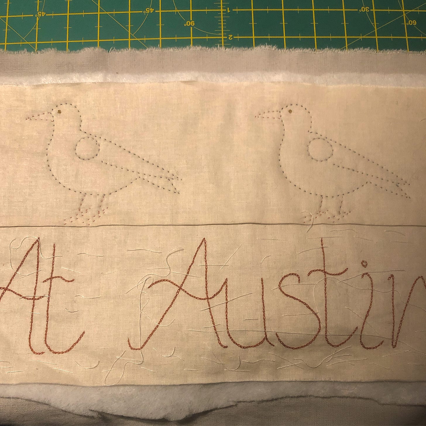 Two birds quilted on to fabric the words “At Austin” embroidered below.