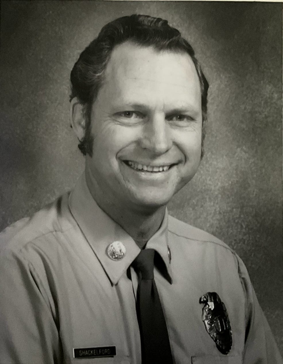 A black-and-white portrait of a middle-aged white man wearing an LA County Fire Department uniform.