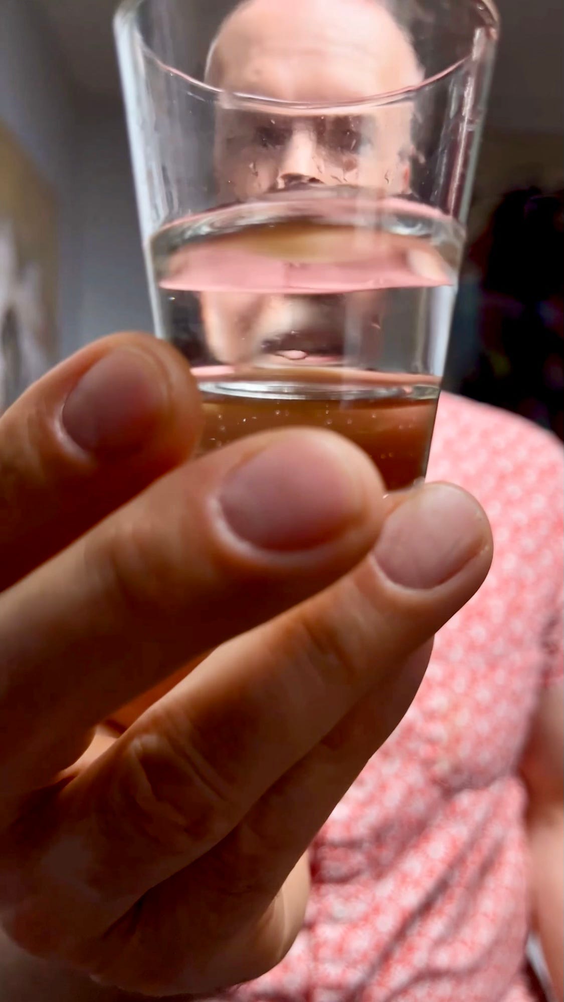 A man holds up a shot glass with a little water in it. 