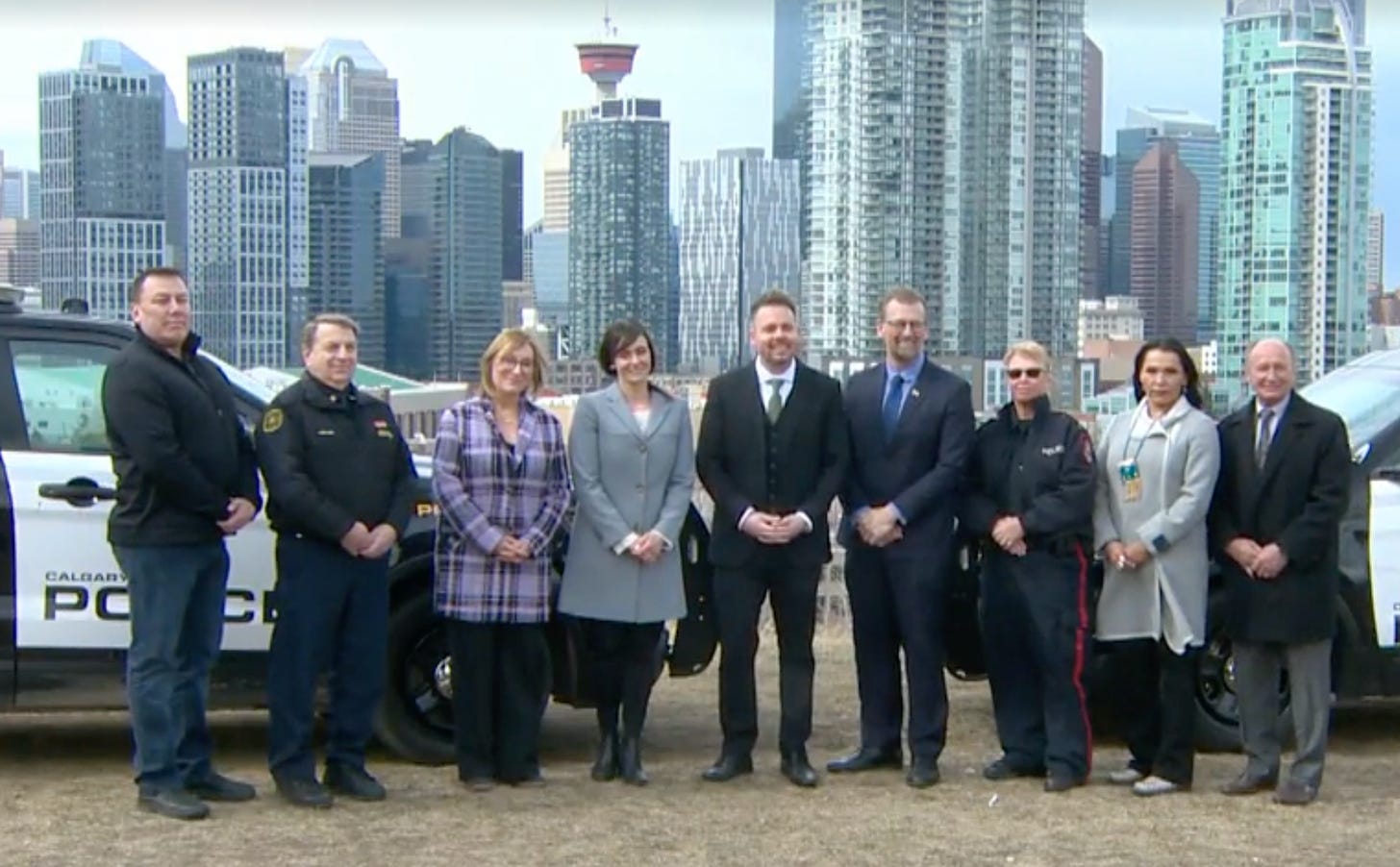 Group of police and politicians gather in front of police cars to make an announcement in front of Calgary downtown