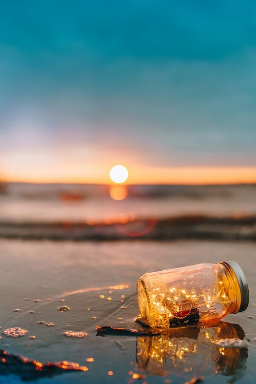 a bottle with gold trinkets on a beach.