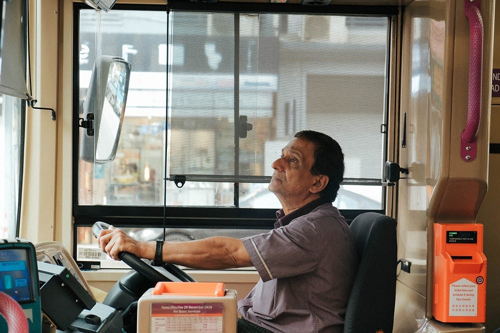 Photo of a bus driver, with a coin collector ticketing machine in the foreground