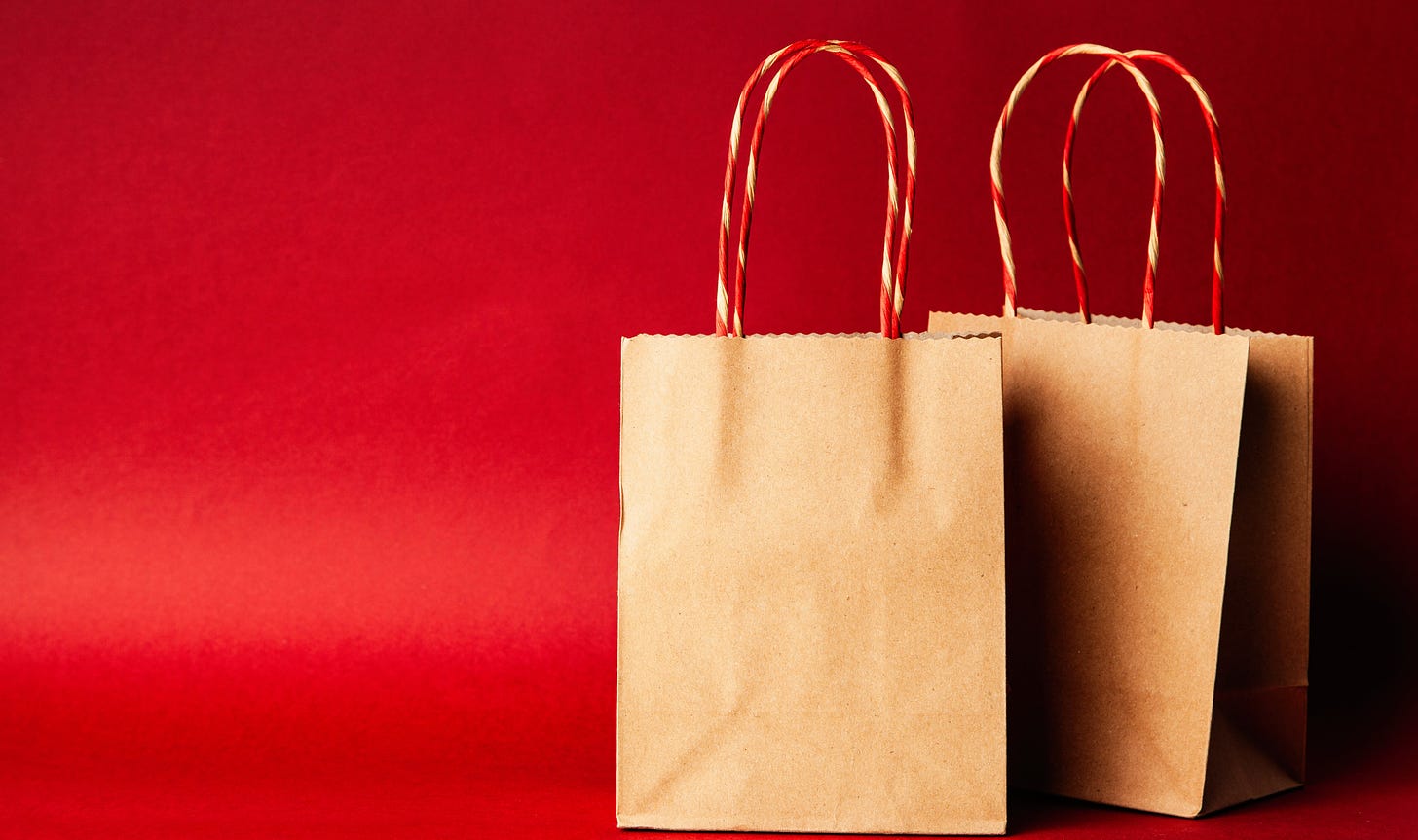 Two paper shopping bags against a dark red background
