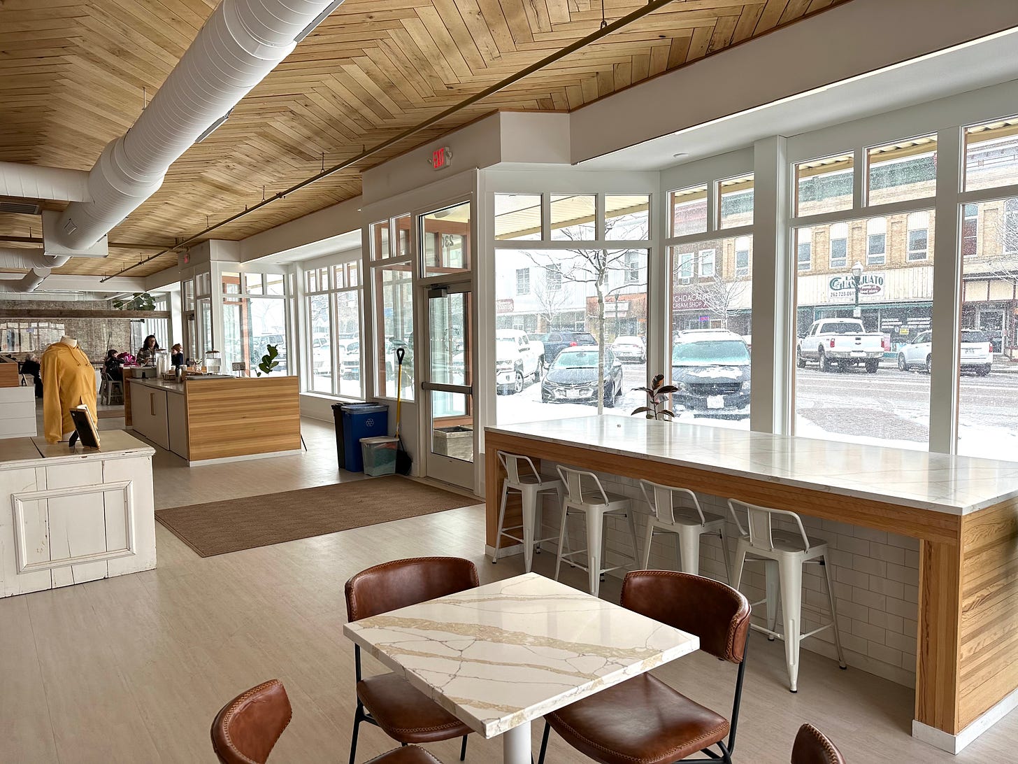 Interior of a coffee shop with chairs and countertops looking out through glass windows at the snow covered cars and street.