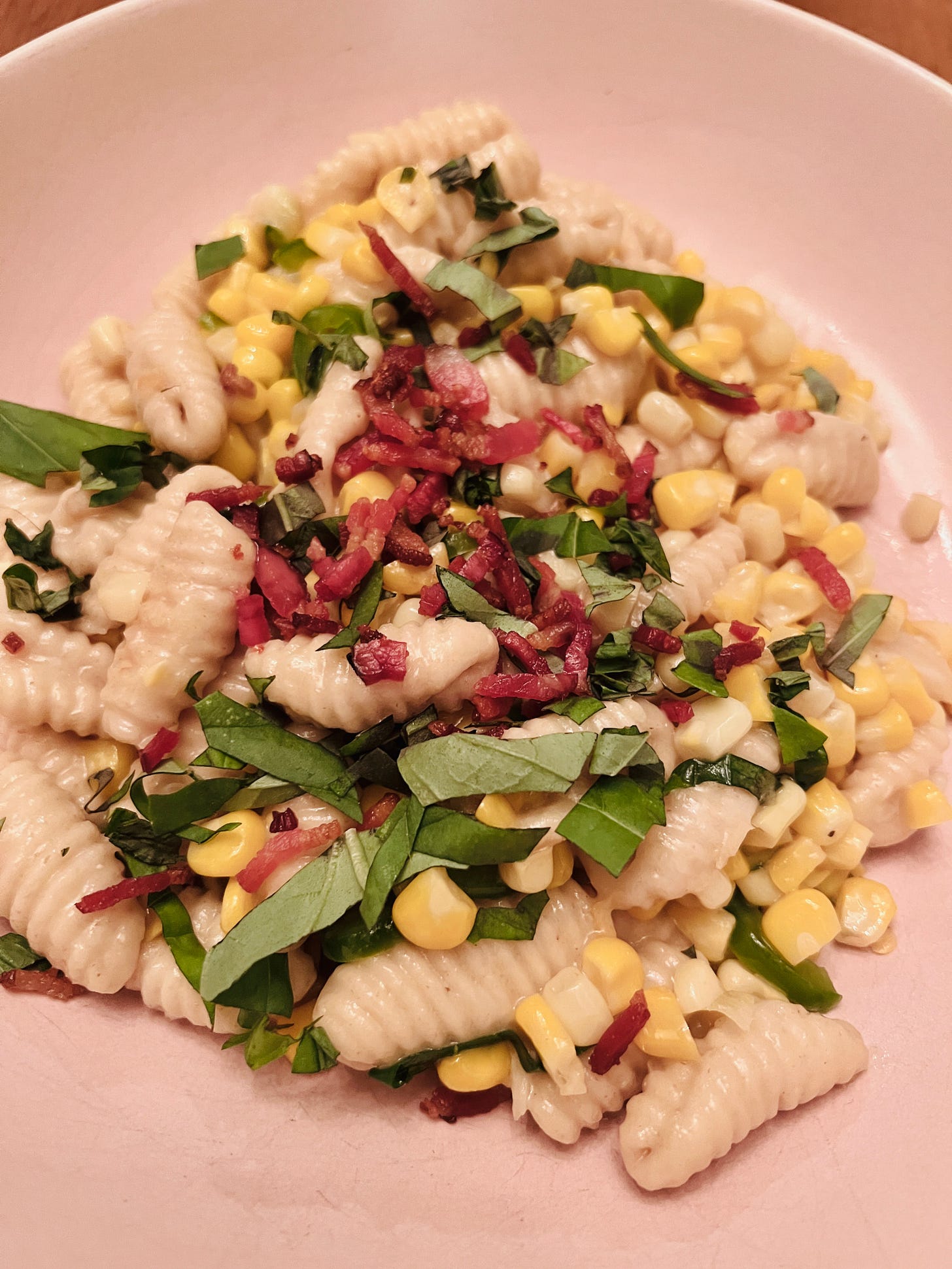 a bowl of pasta with corn, basil, and crispy bacon bits