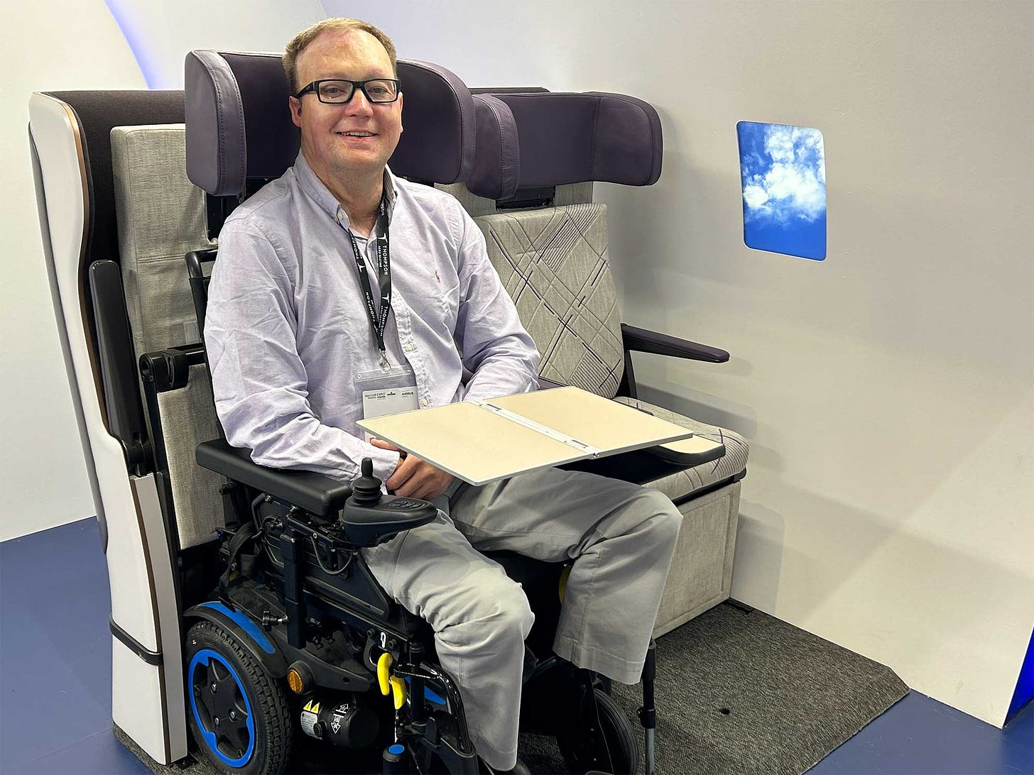 John seated in a power wheelchair in a wheelchair securement space prototype for airplanes.
