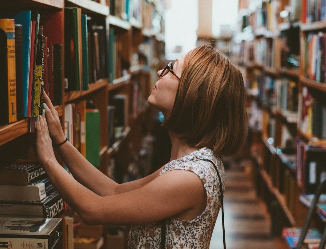 woman standing between library book shelves woman standing between library book shelves