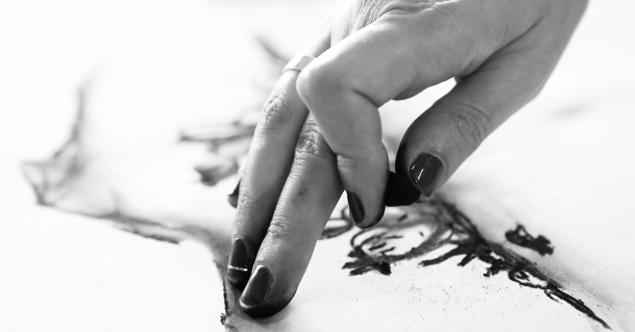 Black-and-white close up of a hand smudging a charcoal line drawing