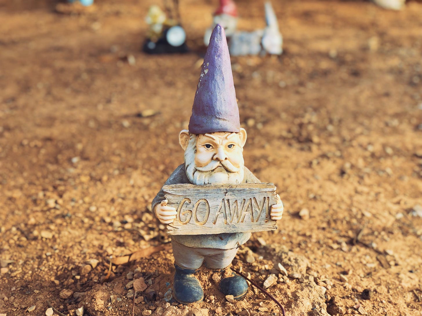 Photo of a garden gnome holding a sign that says "go away" in all caps
