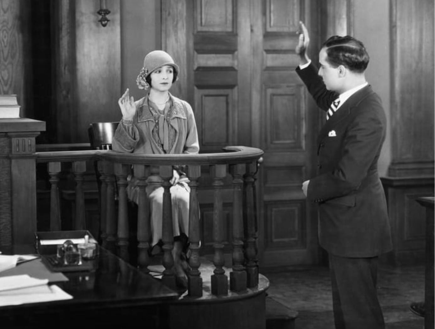 Black & white photo of woman being sworn in as witness in court proceeding.
