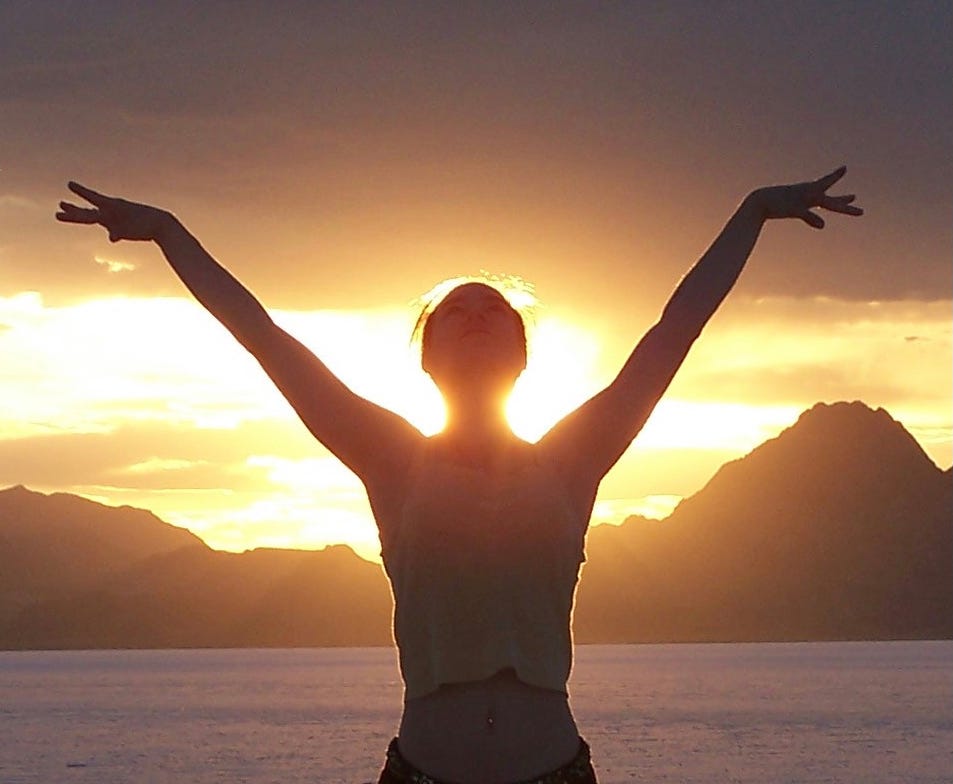 Me: standing in silhouette before the mountains with the setting sun ablaze at my back. My arms and head are lifted in a power pose.