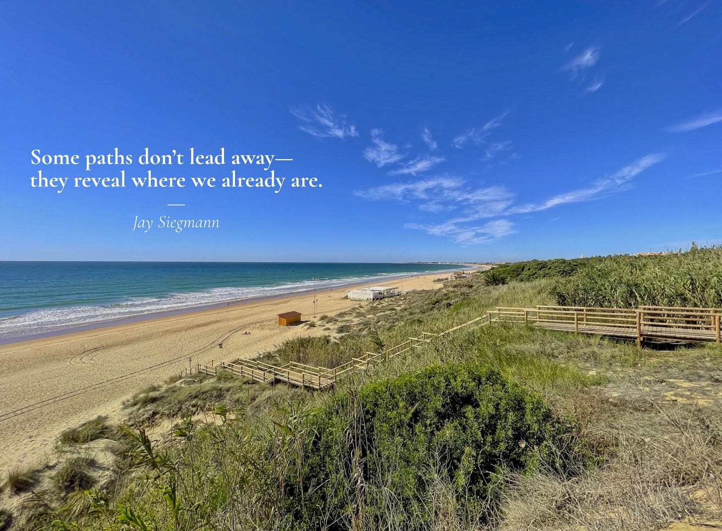Wide-angle view of La Barossa beach and Periurban Park in Andalusia, Spain. A wooden boardwalk winds through dry coastal vegetation toward the sandy shore. The ocean stretches calmly under a clear blue sky with soft, feathered clouds drifting above the horizon. Wide-angle view of La Barossa beach and Periurban Park in Andalusia, Spain. A wooden boardwalk winds through dry coastal vegetation toward the sandy shore. The ocean stretches calmly under a clear blue sky with soft, feathered clouds drifting above the horizon.