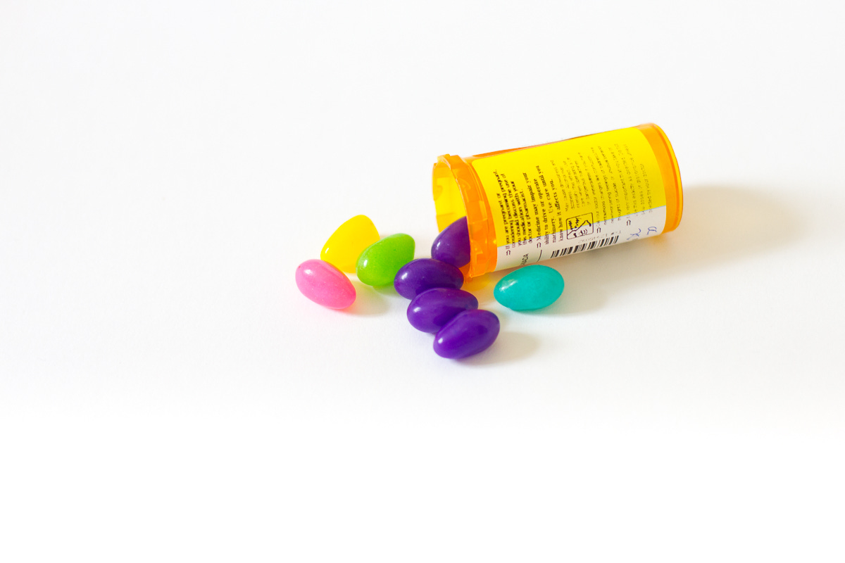 prescription pill bottle with jelllybeans falling out of it, against plain white background