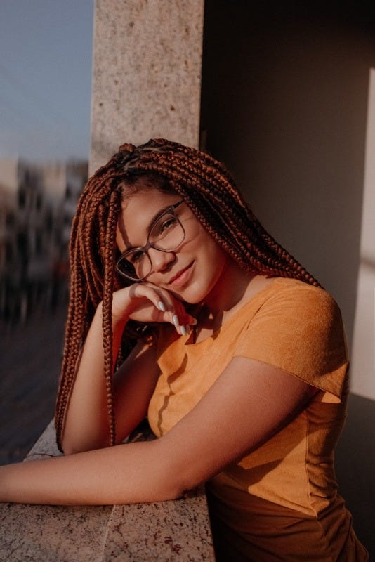 Person with glasses and braids leaning on a balcony smiling