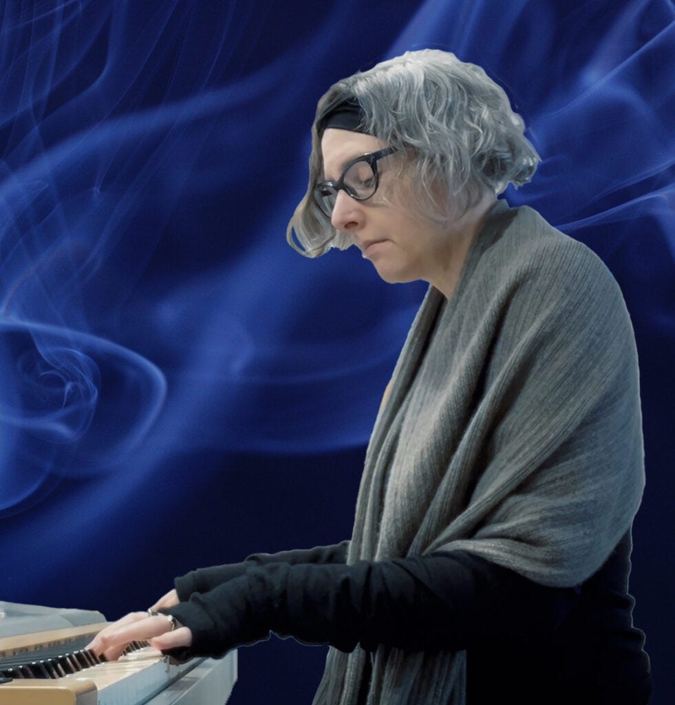 Lia Pas, a white woman with grey hair and a blackand grey outfit, plays a digital piano against a swirling dark blue background.