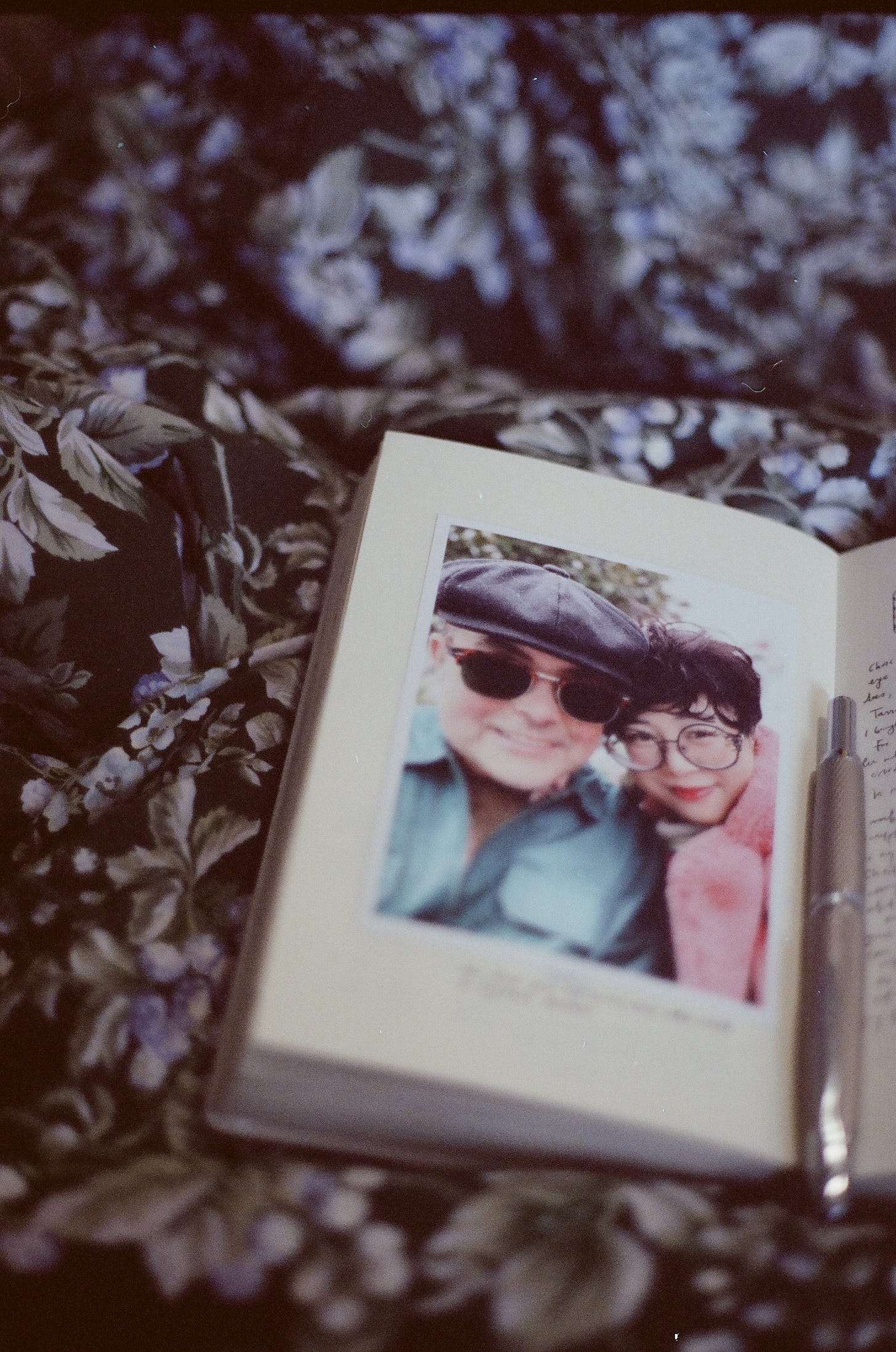 photo of a man in a newsboy cap and a woman with short curly black hair, heads leaned together. they are similing outdoors and the photo is pasted into a journal
