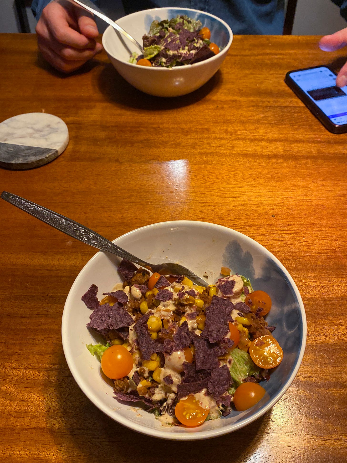 Two white and blue bowls of the taco salad described above, with blue corn chips crumbled on top, and orange cherry tomatoes sliced in half sprinkled throughout. 