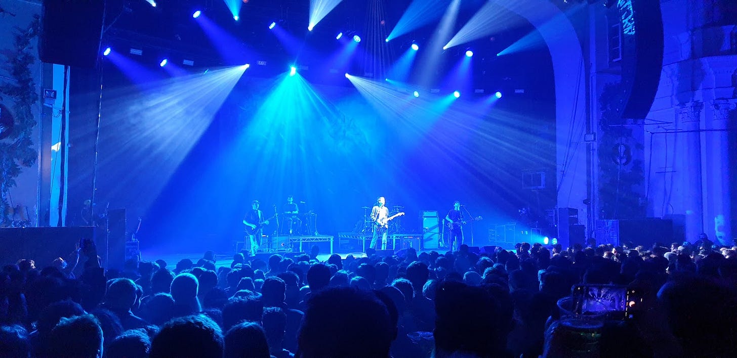 Blue stage lighting illuminating performers at O2 Academy Brixton with the crowd silhouetted in the foreground