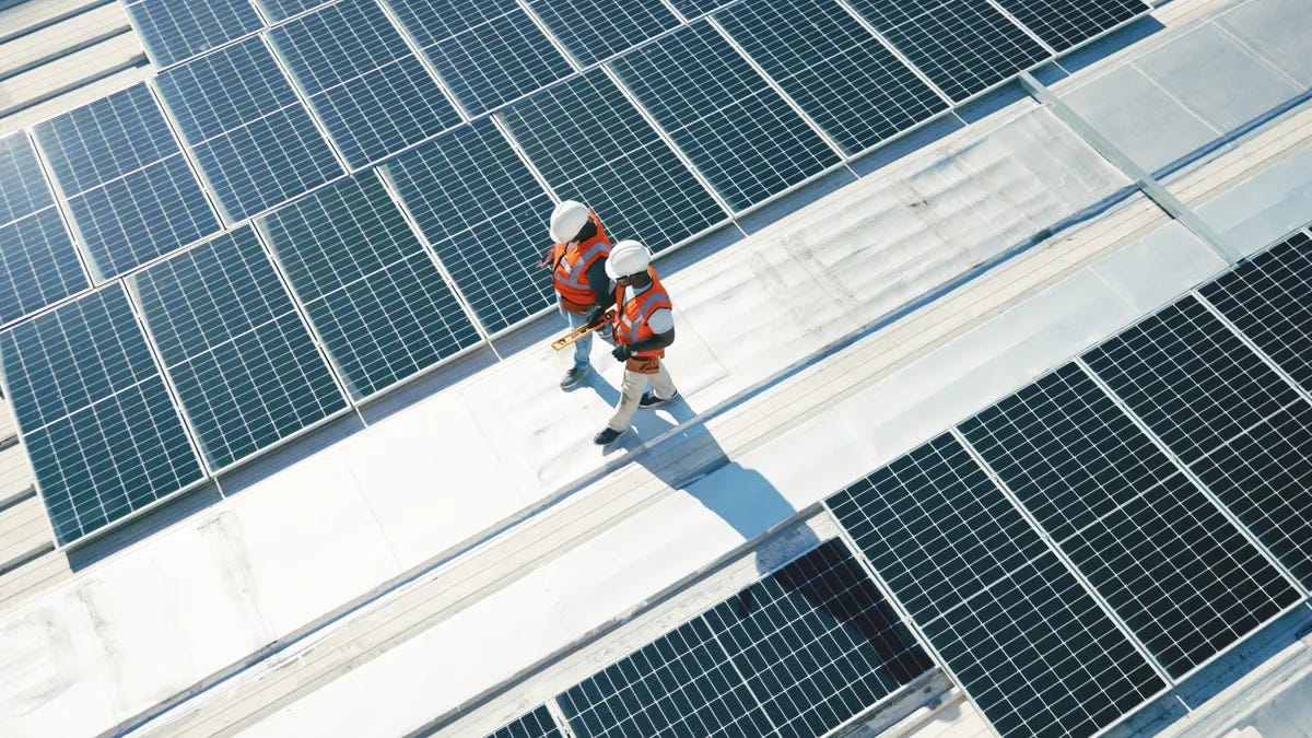 Aerial shot of two people in hard hats walking on a rooftop between solar panels