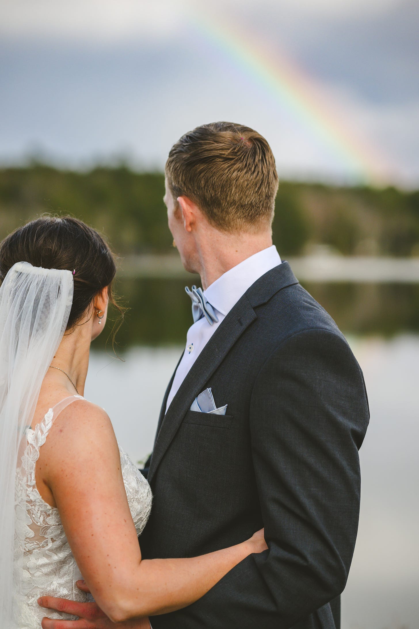 A bride and groom turning to look at a beautiful rainbow