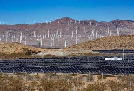 solar panels in foreground, wind turbines in background in desert