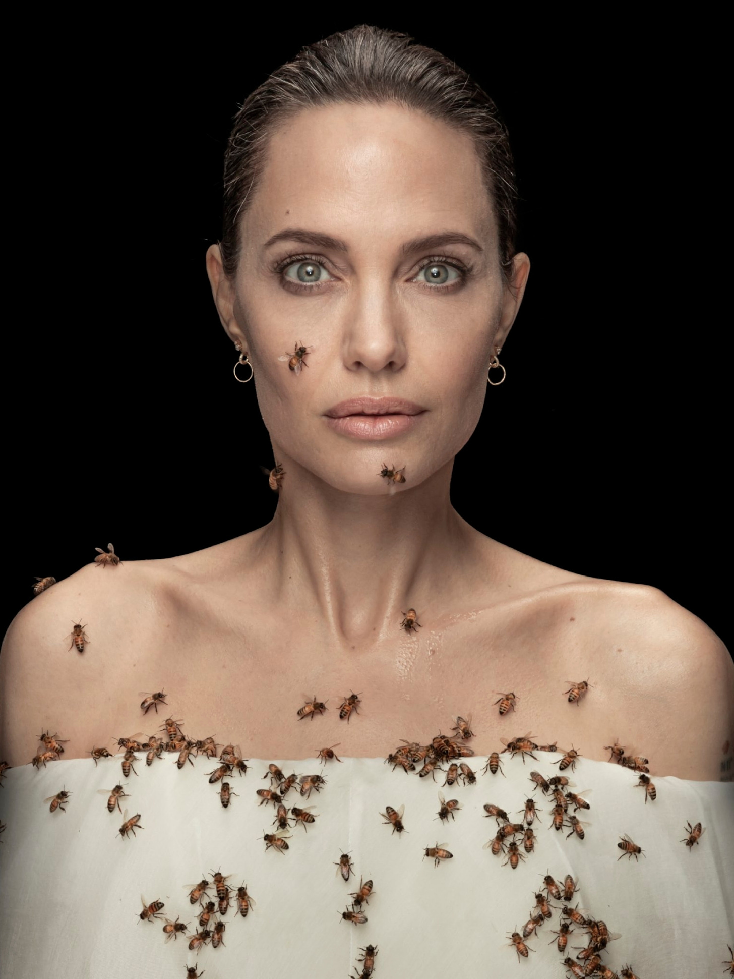 a studio portrait of Angelina Jolie with a group of bees resting on her