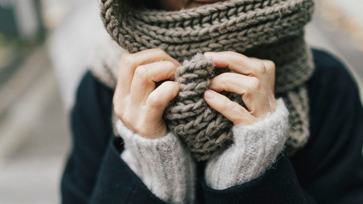 a woman wearing many layers clutches her scarf in her hands