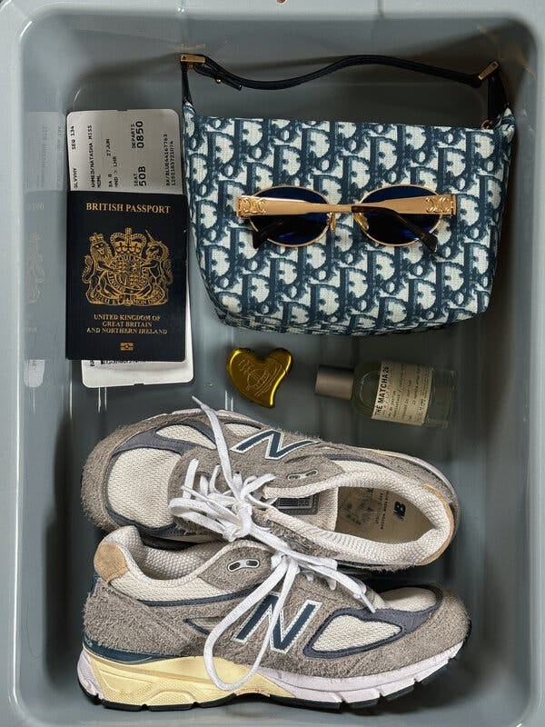 A gray bin with shoes, a perfume, a passport, a purse and gold glasses in it.