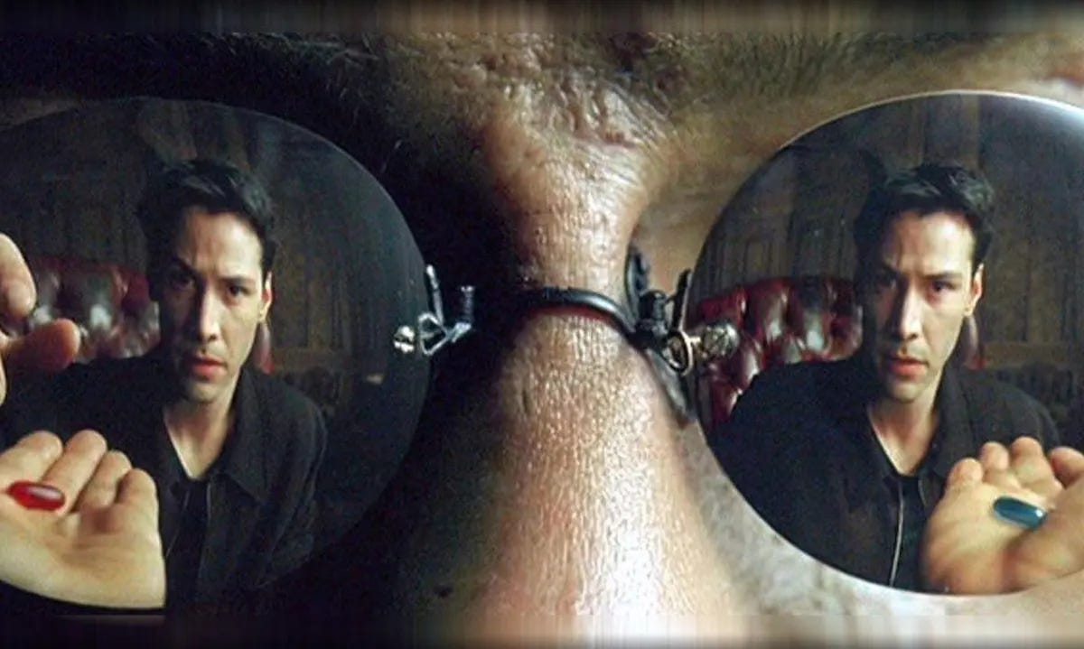 Extreme close-up of a Black man's face. It is zoomed in from his brow to mid-nose, with the focus on mirrored sunglasses which reflect a man looking at the viewer while in front of an outstretched hand in each lens. The hand on the left holds a red pill and the right hand holds a blue pill. The man's reflection on the left is reaching for the red pill.