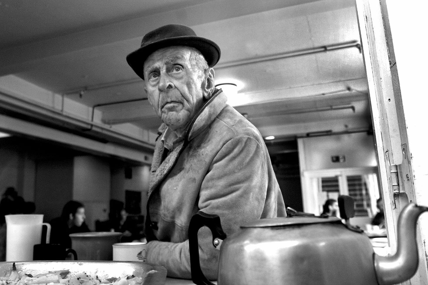 A black and white photo of a man called William. Unwashed and wearing a sheepskin coat and a porkpie hat, I photographed William while serving tea in a Northampton homeless shelter. William told me it was his birthday and would like an extra spoon of sugar in his tea. No Idea if it was his birthday but I wished him a happy one and gave him two extra. 