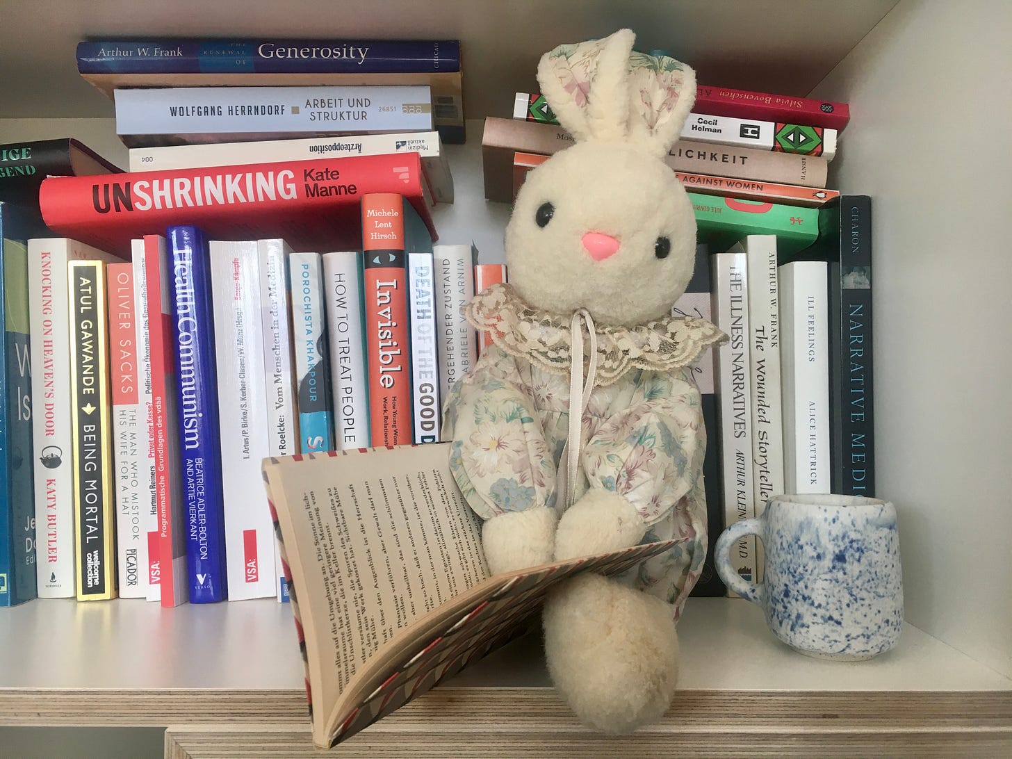Ein Kuschelhase sitzt in einem Bücherregal und liest, daneben steht eine kleine Tasse.