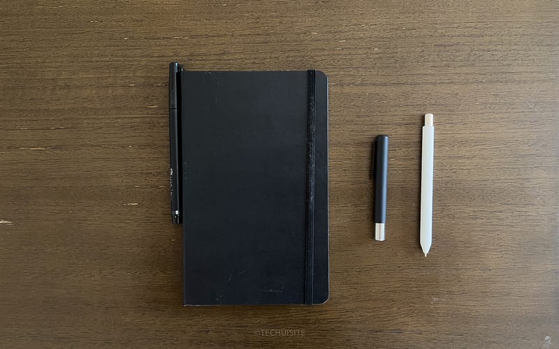 Moleskin and Studio Neat writing tools (Mark Two and Mark Three) on brown table.