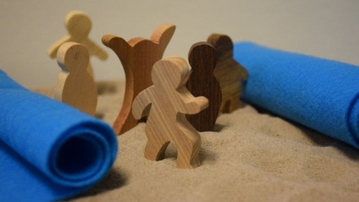 Small wooden figures stand in sand with blue felt rolled back on either side as part of the Exodus story