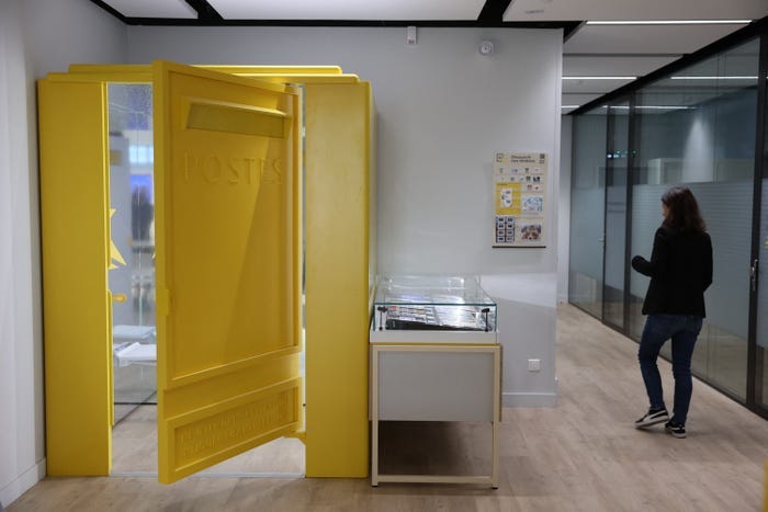 A woman stands near a retry booth set up in a La Poste French post office to allow people to try on clothes purchased on the internet in Paris, on January 10, 2024. Try on a piece of clothing purchased online in a post office and possibly return it immediately: La Poste is experimenting with fitting rooms in a few agencies in France, upsetting certain traders who point to "serious risks" for "local shops".