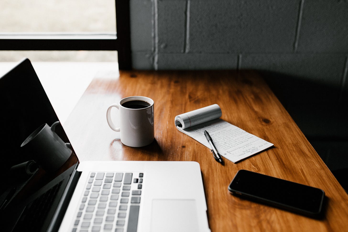 Laptop and mobile phone on a table with a mug, notes and a pen