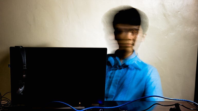 A blurred picture of a man, looking at a laptop and shifting back and forth. The head is blurry from moving back and forth.