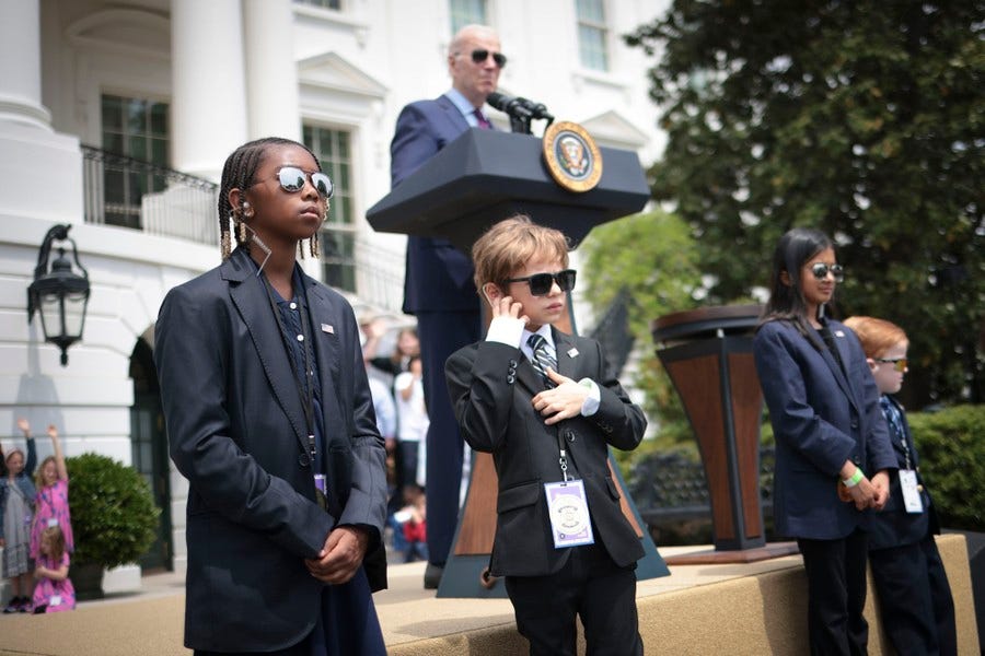 Several children dressed as Secret Service agents stand in front of a lectern as President Joe Biden speaks.