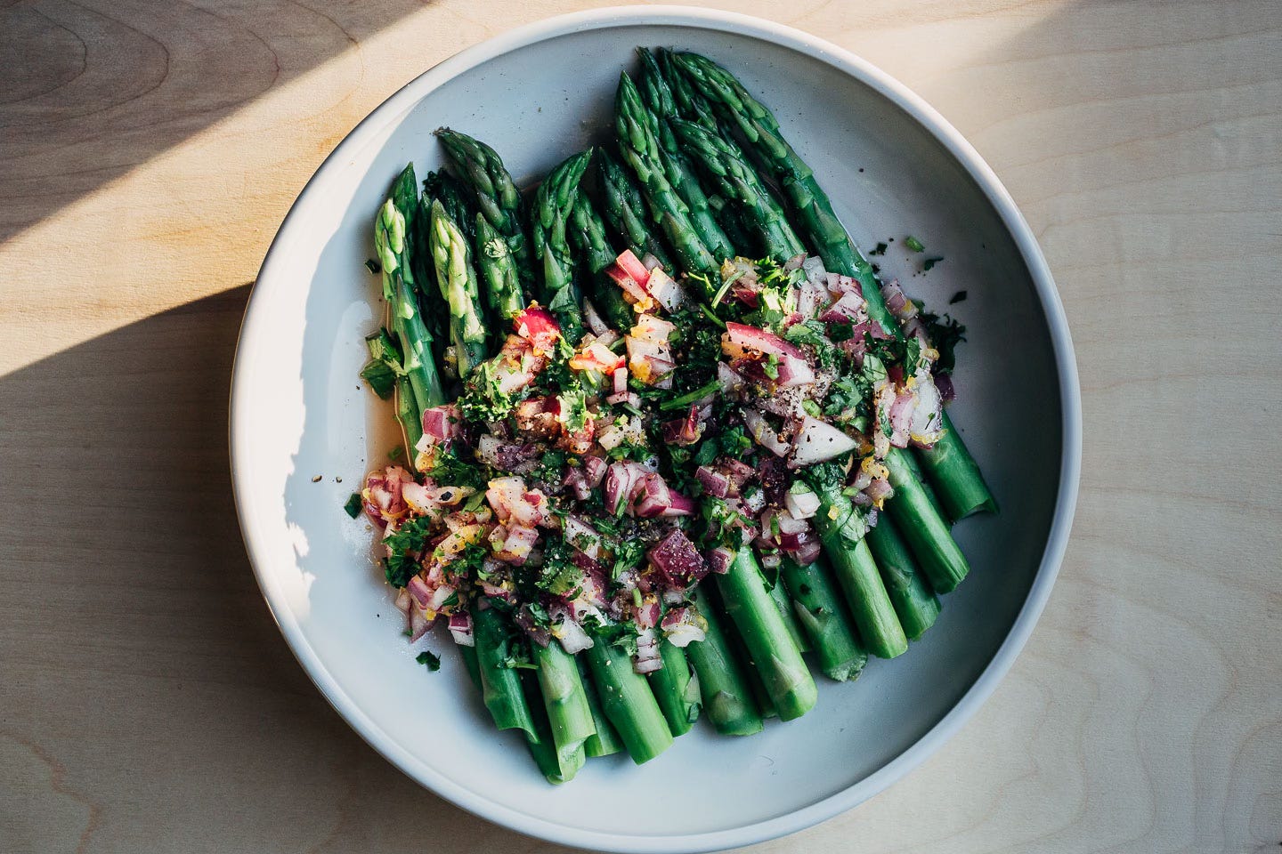 Cold asparagus salad in a shallow bowl. It’s topped with red onion relish and herbs. 