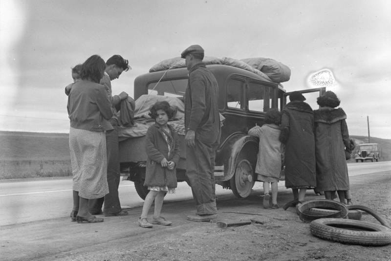 A vintage black and white image of a family of adults and children standing around and entering a car.