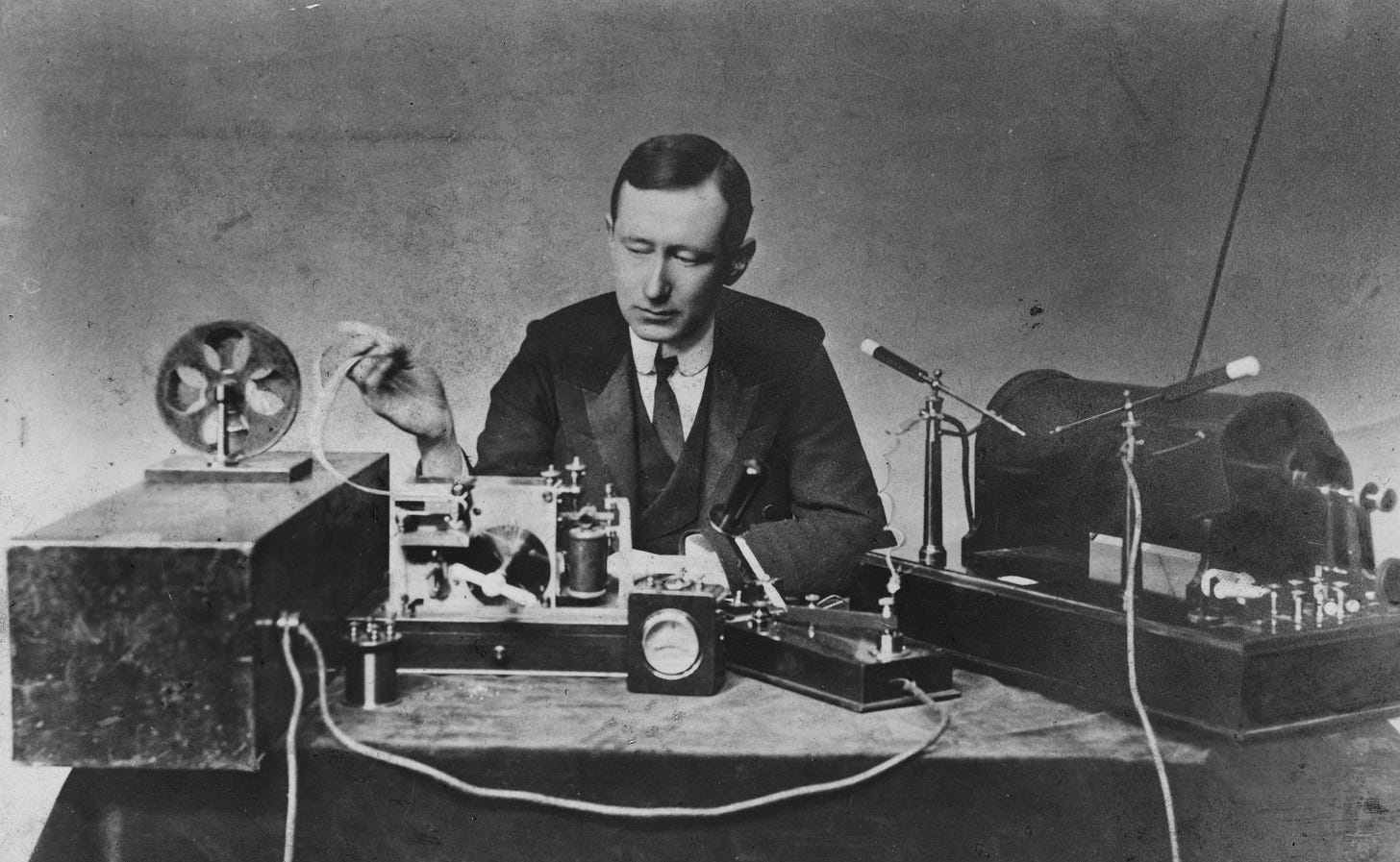 Black and white photo of a man next to a steampunkish early radio.