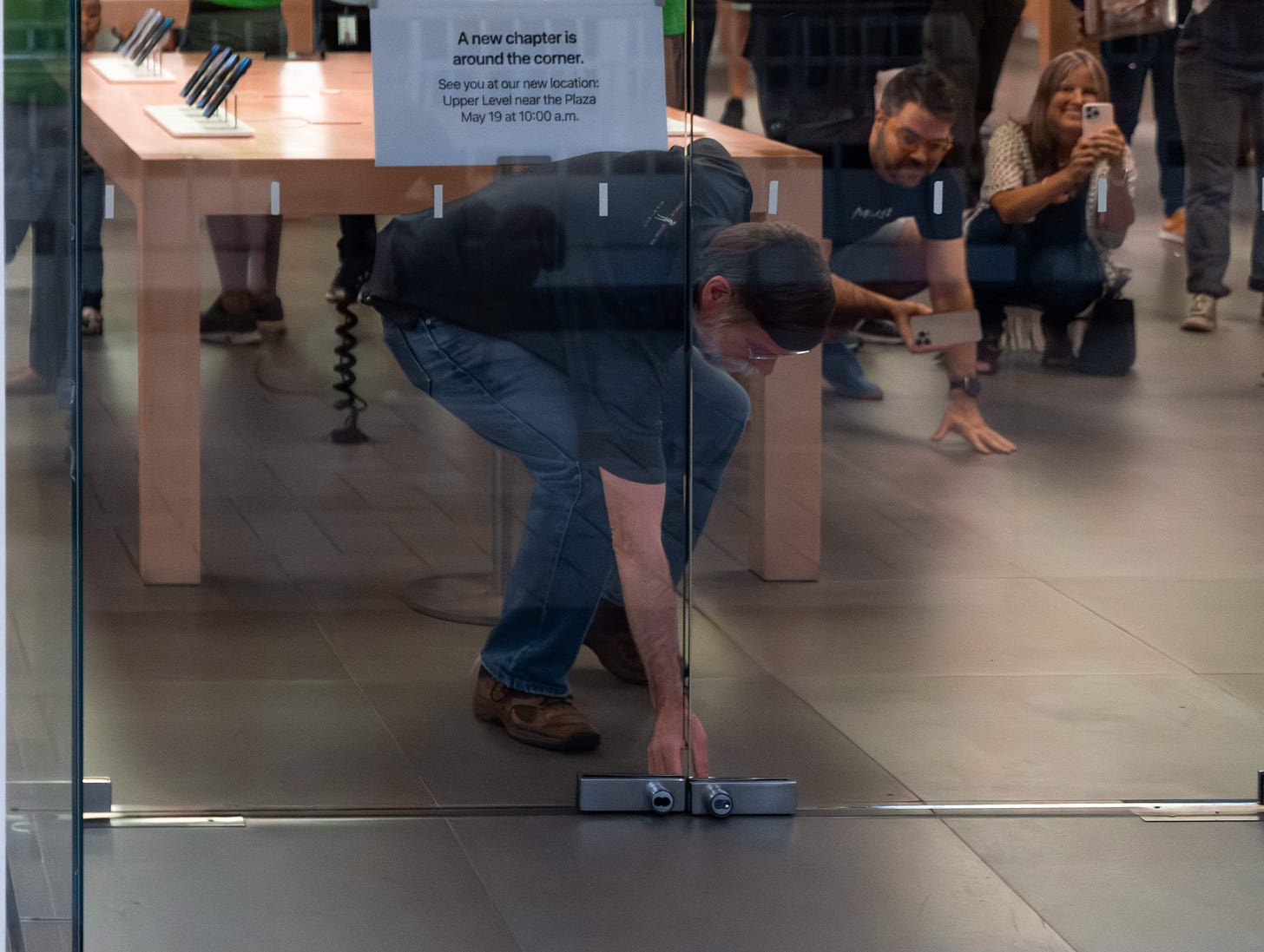 A store employees locks the doors at Apple Tysons Corner on the store's last night of service before moving to a new location. An easel behind the employee says "A new chapter is around the corner."