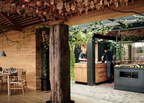 Two chefs cooking in an open-air kitchen, decorated with leaves.
